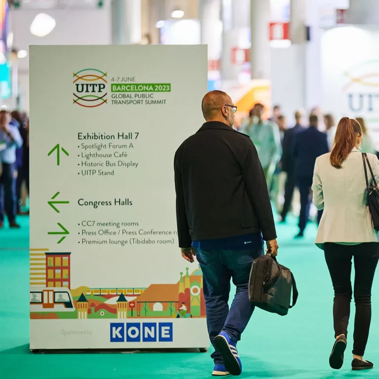 Visitors walking past sponsored signage at the UITP Summit.